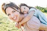 Mature woman giving daughter piggy back ride in park