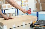 Hands of warehouse worker taping parcel in distribution warehouse