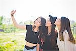 Three young female friends puckering lips for smartphone selfie in park