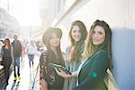 Portrait of three young women using digital tablet on city street