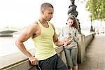 Male and female runners texting on smartphone at riverside