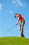 Low angle view of golfer on hill wearing sun visor holding golf club