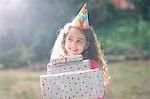 Girl carrying stack of gifts at garden birthday party