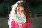 Portrait of girl crossing eyes with lollipop in front of her face in garden