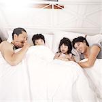 Young Chinese family of parents and two young children laying in bed together at home