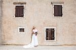 Bride in wedding dress standing in front of old house