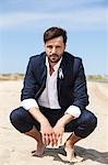 Groom crouching on beach