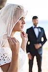 Bride adjusting veil, groom in background