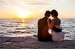 Bride and bridegroom sitting on pier at sunset