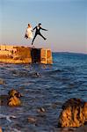 Bride and groom on pier jumping into the air