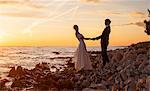 Bride and groom holding hands against sunset