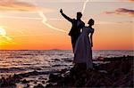 Bride and bridegroom taking photo of themselves at sunset