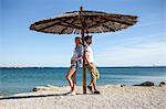 Young couple standing under parasol on beach