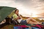 Young woman at campsite drinking cup of coffee