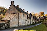 The midday sun casts its light across a row of medieval houses at Arlington Row, Bibury in Gloucestershire, Cotswolds, England, United Kingdom, Europe