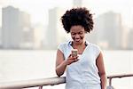 A woman leaning on a waterfront rail checking her cell phone