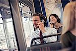 Two people seated on a bus talking on their cell phones
