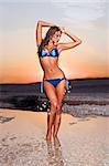 beautiful woman in a bathing suit standing on the beach at sunset