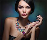 portrait of a glamorous girl with black hair and an expensive necklace with precious and colored stones
