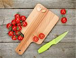 Cherry tomatoes with knife on cutting board over wooden table background