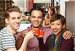 Group of three adults toasting coffee mugs in cafe