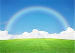 Green grass field, blue sky with clouds on horizon and rainbow background