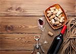 Red wine bottle, wine glass, bowl with corks and corkscrew. View from above over rustic wooden table background