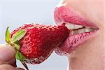 Seductive woman with red lips eating a fresh strawberry