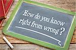 How do you know right from good - ethics question on a slate blackboard with a white chalk and a stack of books against rustic wooden table