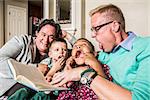 Homosexual parents reading and making faces with son and daughter