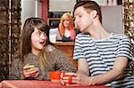 Woman holding phone as boyfriend looks over in cafe