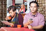 Young distracted African American couple using digital devices in cafe