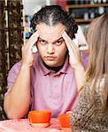 Stressed out man rubbing his head at table with friend