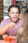 Angry man yelling and pointing at woman in cafe