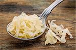 tablespoon of sauerkraut against rustic wooden cutting board - healthy eating concept