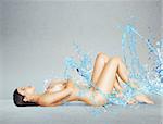 Naked woman lying with splashing blue water