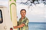 Optimistic man with eyeglasses holding a surfboard in Hawaii
