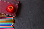 Set of colorful pencils with old booak and apple on black board
