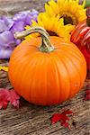 one orange pumpkin with flowers and fall leaves on wooden textured  table