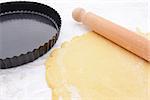 Loose-bottomed baking tin next to rolled out shortcrust pastry and rolling pin