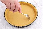 Woman uses metal fork to prick ventilation holes in an uncooked pie crust