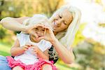 Cute Little Girl With Mother Making Heart Shape with Hands Outdoors.