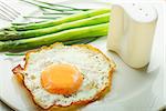 Fried egg with green asparagus on white plate