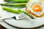 Fork with green asparagus and fried egg on white plate