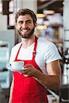 Handsome barista holding a cup of coffee at the cafe