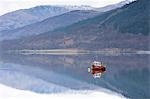 Flat calm Loch Levan with reflections of snow-capped mountains and small red fishing boat, Glencoe Village, near Fort William, Highland, Scotland, United Kingdom, Europe