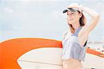 Mid adult woman on beach, holding surfboard