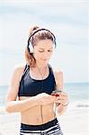 Mid adult woman standing on beach, wearing headphones, looking at mp3 player