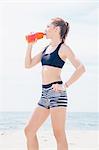 Mid adult woman standing on beach, drinking drink from plastic bottle