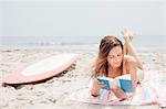 Mid adult woman lying on beach, reading book